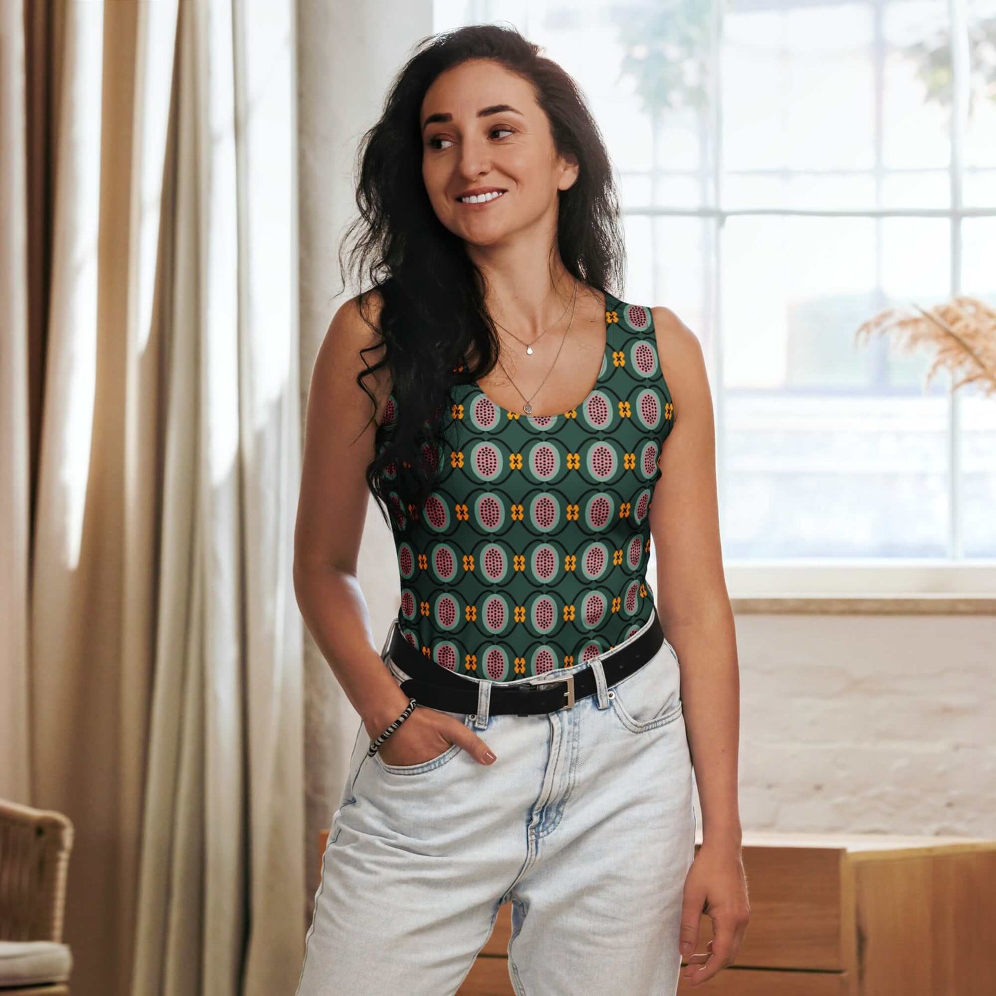 Woman wearing a patterned dark green tank top and light jeans indoors.