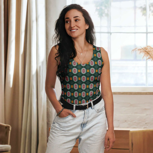 Woman wearing a patterned dark green tank top and light jeans indoors.