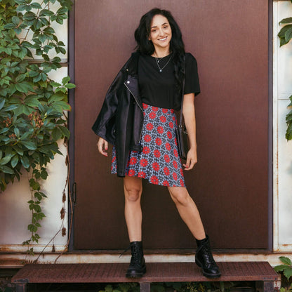 Woman in a red floral skater skirt, black jacket, and black top, standing against a brown door.