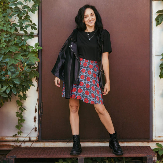 Woman in a red floral skater skirt, black jacket, and black top, standing against a brown door.